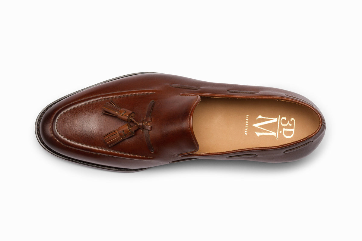 Brown leather tassel loafers styled flat lay on wood surface