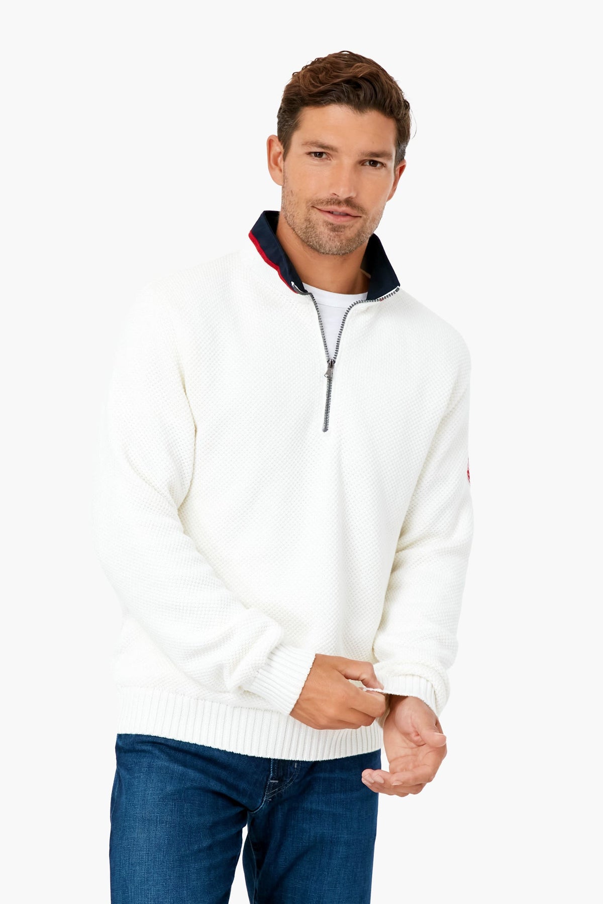 A man wears a white ORYNESTA windproof quarter-zip sweater paired with blue jeans, highlighting classic Scandinavian knitwear style.