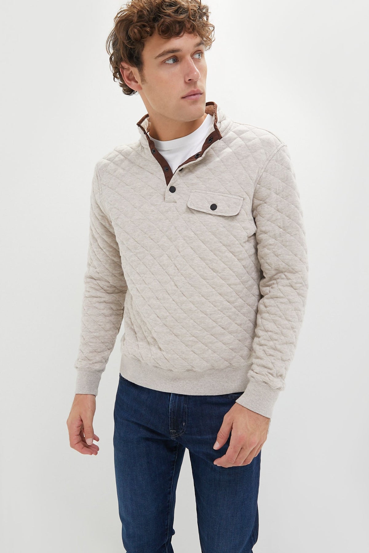 A man wears a light beige ORYNESTA  Fleece Pullover with a chest pocket and blue jeans, highlighting this sustainable essential.